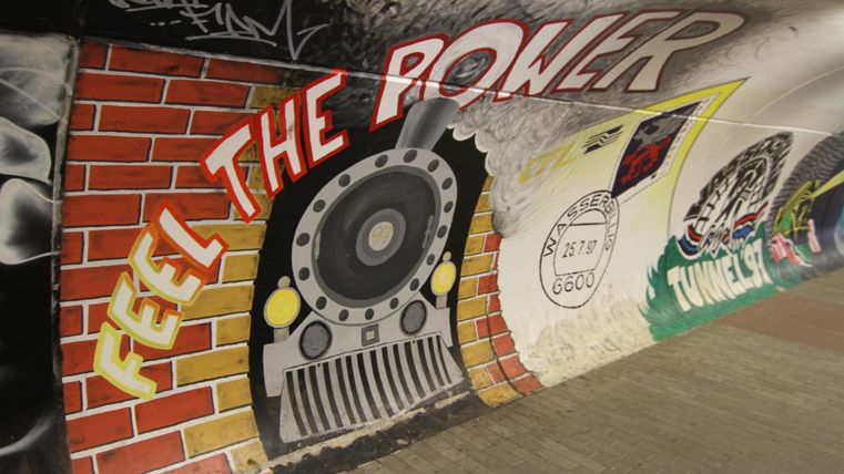 Ein grafisches Wandbild mit einem Dampflok-Motiv und der Aufschrift „FEEL THE POWER“. Die Farben sind lebhaft und das Design vermittelt eine dynamische Atmosphäre.