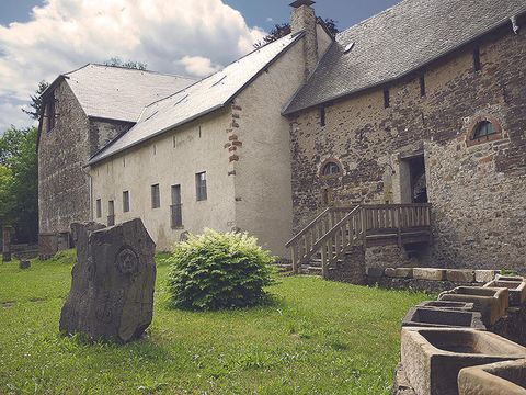 Historical building with stone wall, wooden staircase, and green surroundings. Old stone sculptures in the foreground.