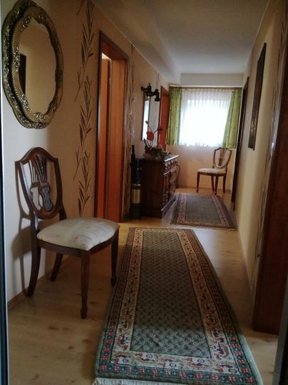 Ein einladender Flur mit Holzfußboden und einem Teppich. An der Wand hängt ein Spiegel, und es gibt eine Kommode sowie Stühle am Ende des Raumes.