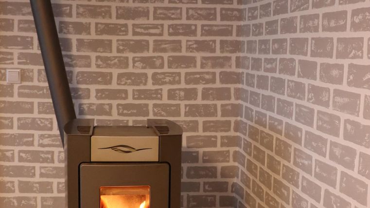 Ein moderner Kaminofen steht in einer Ecke mit einer Backsteinwand. Das Feuer im Ofen sorgt für eine gemütliche Atmosphäre.