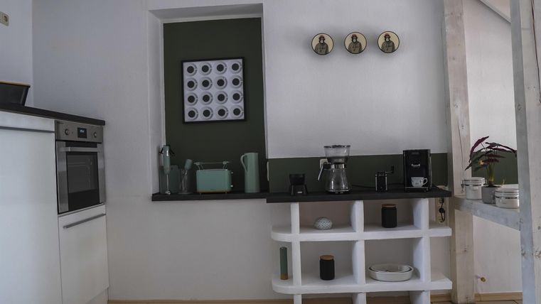 Eine moderne Küche mit weißen Möbeln und einer gemütlichen Atmosphäre. Auf der Arbeitsfläche stehen verschiedene Küchengeräte und Dekorationselemente.