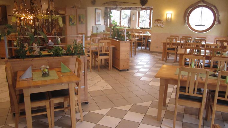 An inviting restaurant with wooden chairs and tables. The walls are bright and decorated with plants.