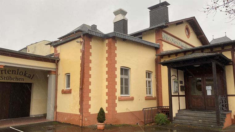 A two-story building with a yellow facade and red accents can be seen. It has a traditional design and is located in a rainy environment.