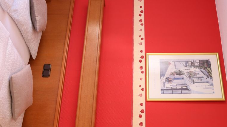 Ein gemütliches Zimmer mit roter Wand und einem gerahmten Bild. Auf dem Bett liegen weiße Kissen.