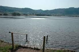 Een stil meer met glinsterend water en zachte heuvels op de achtergrond. De scène straalt een vredige sfeer uit.