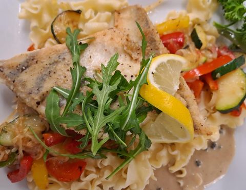 Ein köstliches Gericht mit gebratenem Fisch, frischen Gemüsen und Nudeln. Mit Zitronenscheiben und Rucola garniert.