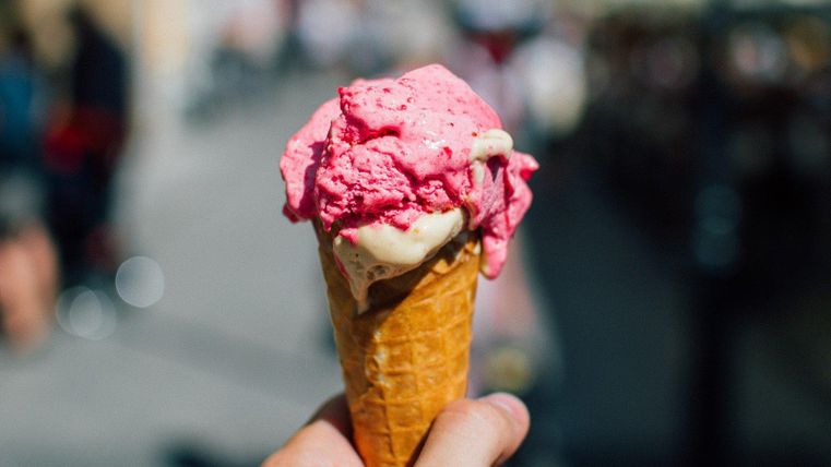 Nahaufnahme eines Eishörnchens mit rosa und beigem Eis, das von einer Hand gehalten wird.