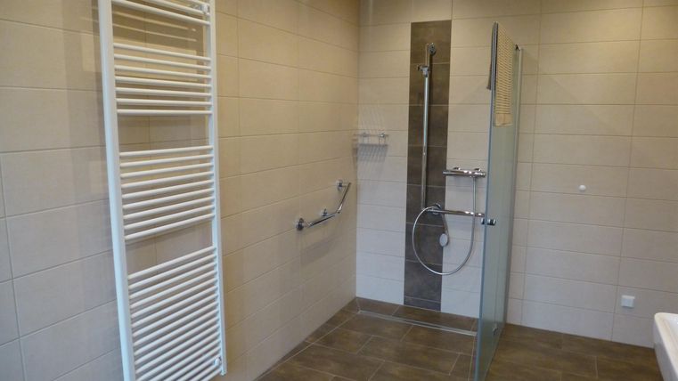 Ein modernes Badezimmer mit einer großzügigen Dusche und einem Handtuchheizkörper. Die Wände sind in neutralen Farben gehalten und schaffen eine helle Atmosphäre.