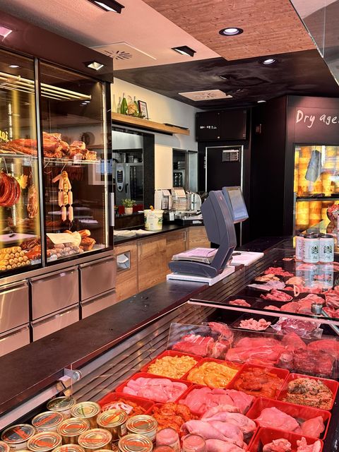 Ein gut sortierter Metzgerladen mit frischem Fleisch und verschiedenen Wurstwaren. Im Hintergrund sind eine Vitrine und Arbeitsflächen zu sehen.