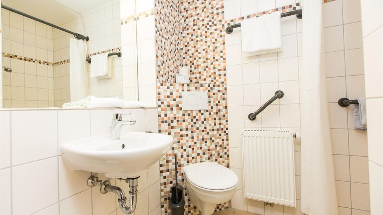 Een moderne badkamer met een witte toilet, een wastafel en een douche. De muren zijn gedeeltelijk betegeld met decoratieve tegels.