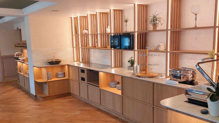 Eine moderne Küche mit Holzregalen und sanfter Beleuchtung. Auf der Arbeitsfläche sind verschiedene Küchenutensilien und eine Mikrowelle sichtbar.