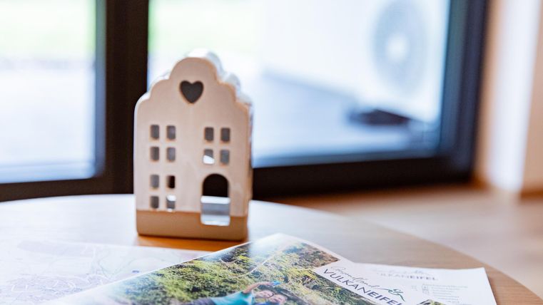 Ein dekoratives Haus aus Keramik steht auf einem Tisch. Daneben liegt eine Zeitschrift über Vulkanreisen.