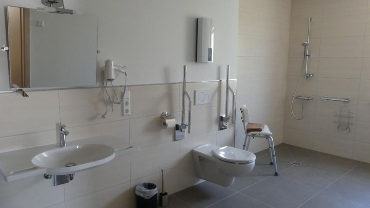 Ein modernes Badezimmer mit zwei Waschbecken und einem behindertengerechten WC. Die Einrichtung ist hell und funktional.