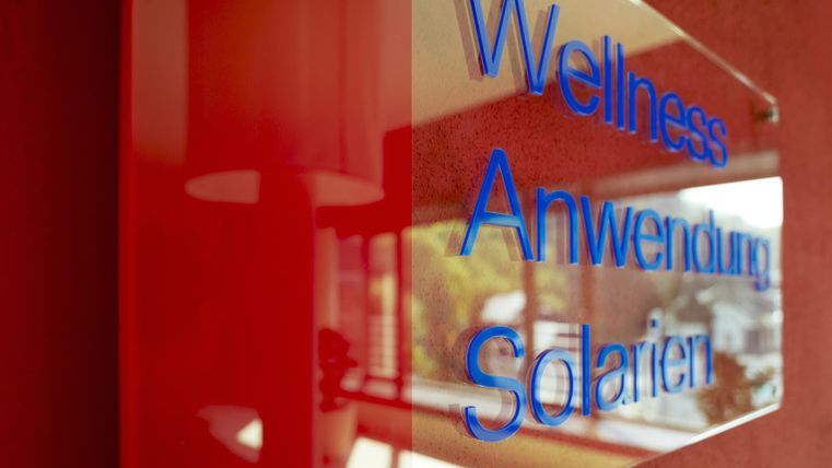 Een bord dat de termen „Wellness“, „Toepassing“ en „Zonnebanken“ toont. De achtergrond is rood en het bord heeft een moderne, elegante uitstraling.