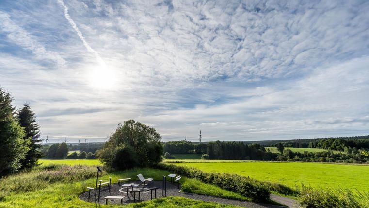 A wide, green meadow under a clear sky with many clouds. In the foreground, there are seating areas, perfect for relaxing and enjoying the view.