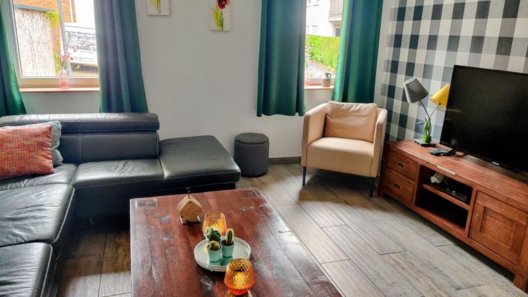 A modern living room with a black sofa and a light armchair. A wooden coffee table stands in the center, surrounded by decorative elements and a television.