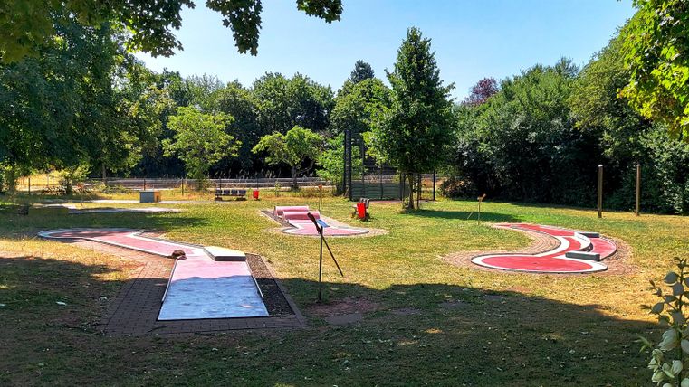 A public park with green grass and various play areas. In the foreground are colorful racetracks visible.