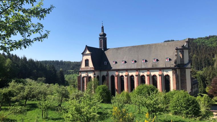 Eine schöne Kirche inmitten von grünen Wiesen und Bäumen. Der Himmel ist klar und blau.