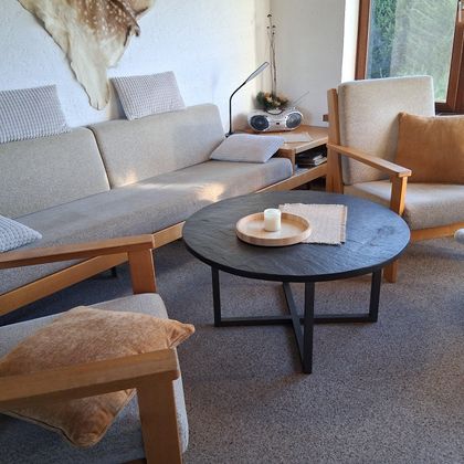 Ein gemütliches Wohnzimmer mit einem hellen Sofa und einem runden Tisch. Die Einrichtung ist modern und einladend, mit natürlichem Licht, das durch das Fenster strömt.