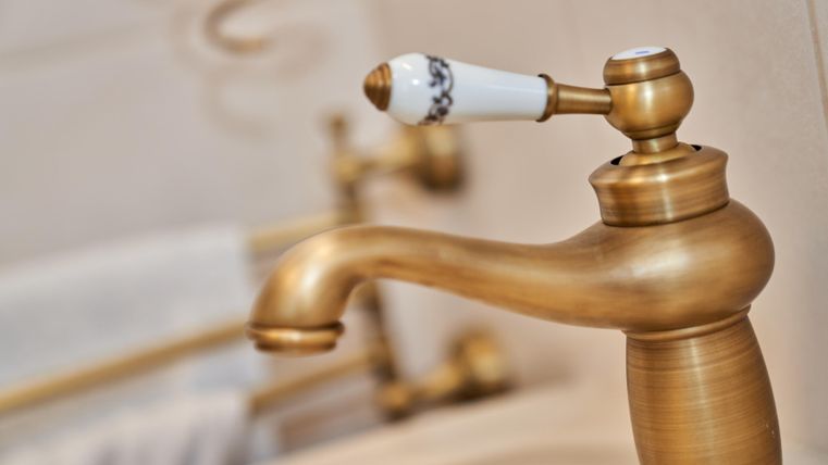 An elegant, gold-colored fixture with a white handle. In the background, soft towels and other bathroom elements are visible.