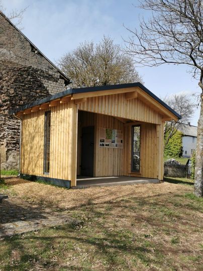 Ein modernes Holzgebäude steht in einem begrünten Bereich. Es hat große Fenster und ein flaches Dach.