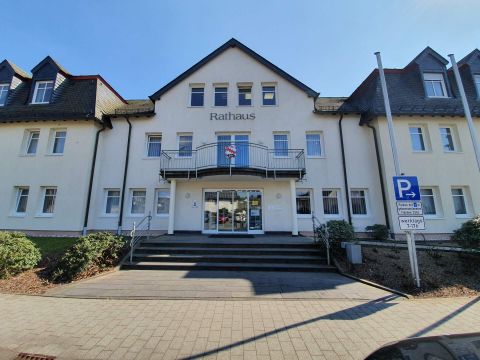 Ein modernes Rathaus mit klaren Linien und einer einladenden Treppe. Im Vordergrund befindet sich ein Parkplatz.