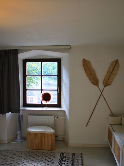 A cozy room with a large window and modern furnishings. Decorative elements made of natural materials hang on the wall.