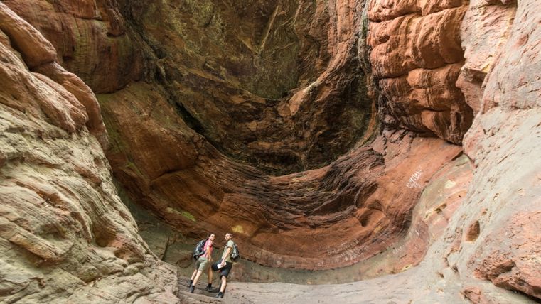 Zwei Wanderer in der Genovevahöhle mit roten Felswänden.