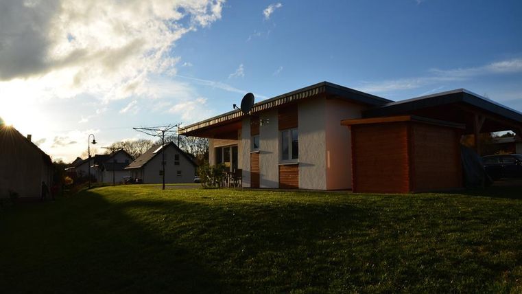 A modern house with a wooden shed and a beautiful garden. The sun is shining in the sky, creating a pleasant atmosphere.