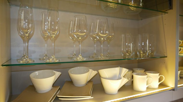 A series of glasses and dishes in a modern glass cabinet. The white cups and bowls are neatly arranged and well visible.