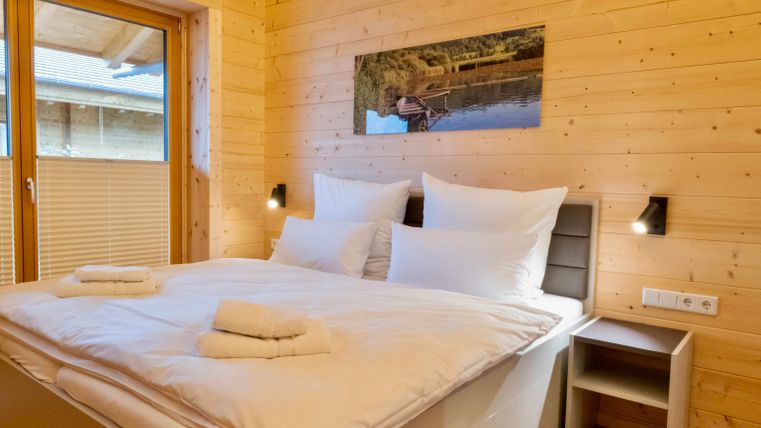 Ein gemütliches Schlafzimmer mit einem großen Bett und frischen weißen Bettbezügen. Die Wände sind aus Holz und es gibt ein Fenster, das viel Licht hereinschickt.