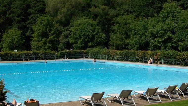 Ein großes Schwimmbecken mit klarem, blauem Wasser. Umgeben von üppigem Grün und Liegen zum Entspannen.