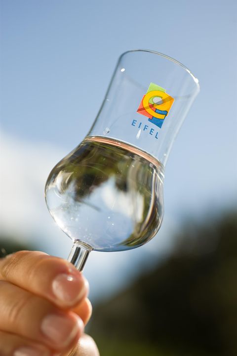 Een glas met water wordt buiten vastgehouden. De lucht is helder en blauw, wat een frisse sfeer creëert.