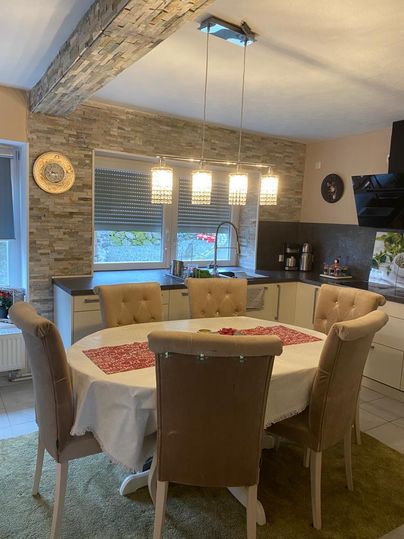 Eine moderne Küche mit einem großen runden Esstisch und bequemen Stühlen. An der Wand sind dekorative Elemente und eine stilvolle Beleuchtung sichtbar.