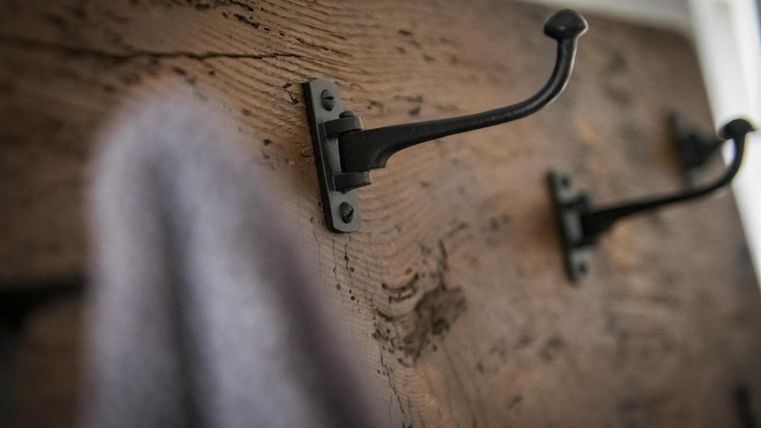Ein Holzbrett mit schwarzen Haken. An einem der Haken hängt ein graues Handtuch.
