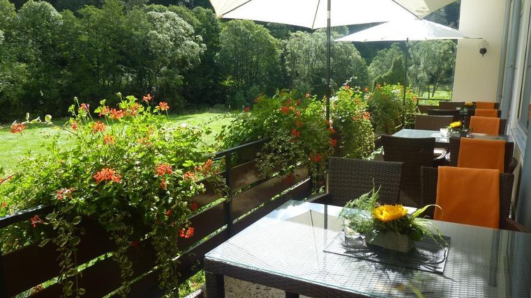 Eine gemütliche Terrasse mit Blumen und Sonnenschirmen. Im Hintergrund ist eine grüne Landschaft sichtbar.