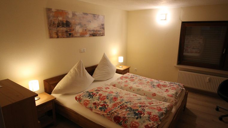 Een gezellige slaapkamer met twee bedden en kleurrijke dekbedden. De kamer heeft moderne verlichting en een groot raam.