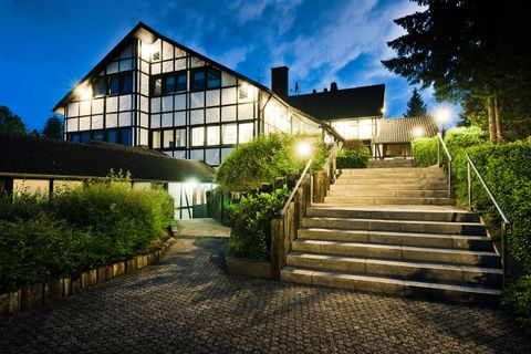 Een modern gebouw met grote ramen, verlicht 's nachts. Een stenen trap leidt naar de ingang, omringd door groene struiken.