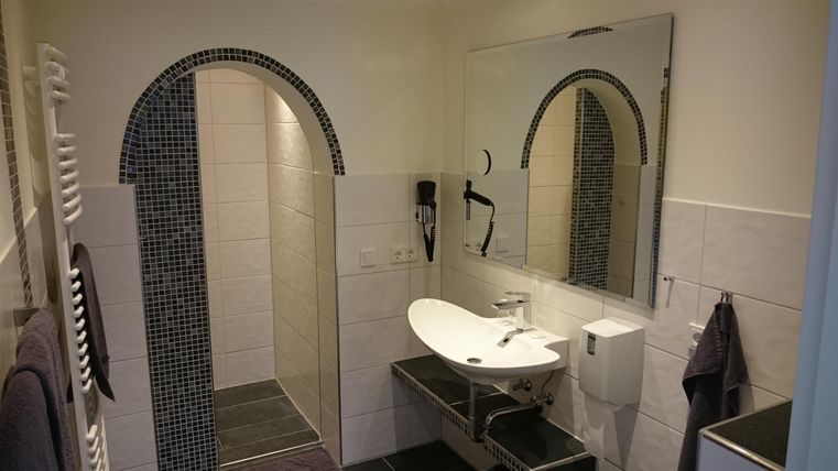 Ein modernes Badezimmer mit einer eleganten Dusche und einem großen Spiegel. Die Wände sind hell gefliest und bieten ein sauberes, frisches Ambiente.