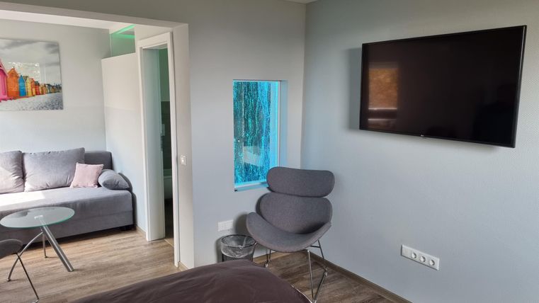 A modern room with a large window and a television on the wall. There is a comfortable sofa and a chair in the corner.