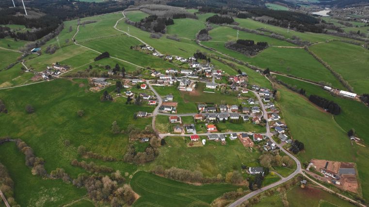 Aerial view of Kerschenbach: Small settlement surrounded by green fields, with numerous wind turbines on the horizon.