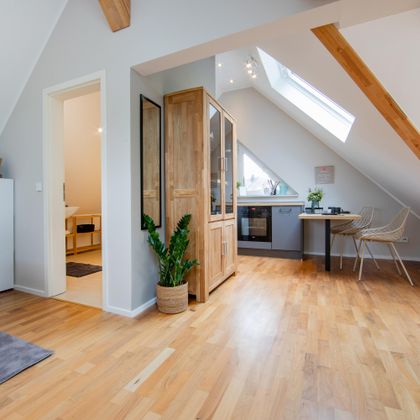 Een gezellige zolderappartement met houten vloeren en een groot raam. De ruimte is licht en modern ingericht.