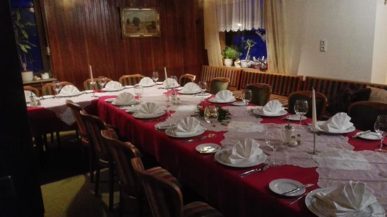 Ein elegant gedeckter Tisch in einem gemütlichen Raum. Die Tischdecke ist rot und die Teller sind liebevoll für Gäste vorbereitet.