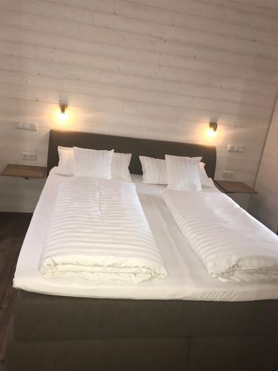 Ein modernes Schlafzimmer mit einem großen Doppelbett. Die Wände sind hell, und es gibt sanfte Beleuchtung an beiden Seiten des Bettes.