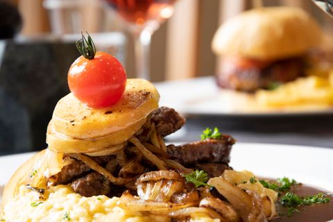 A delicious dish with tender meat, potato slices, and a cherry tomato topping. It is accompanied by flavorful onions and herbs.