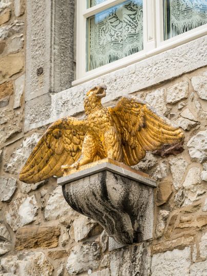 A golden sculpture of a griffin sits on masonry. The griffin has outstretched wings and looks majestic.