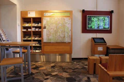 A friendly reception area with maps and informational materials. There are modern furniture and a screen displaying nature images.