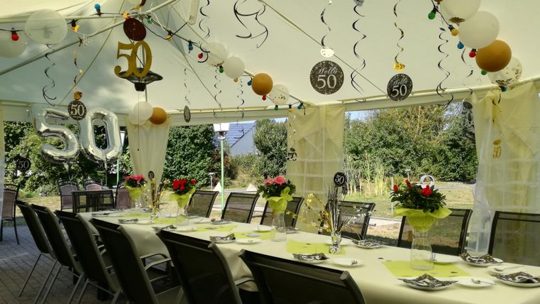 Eine festlich dekorierte Zeltparty für einen 50. Geburtstag. Tische mit Blumen und Ballons sind für die Gäste vorbereitet.