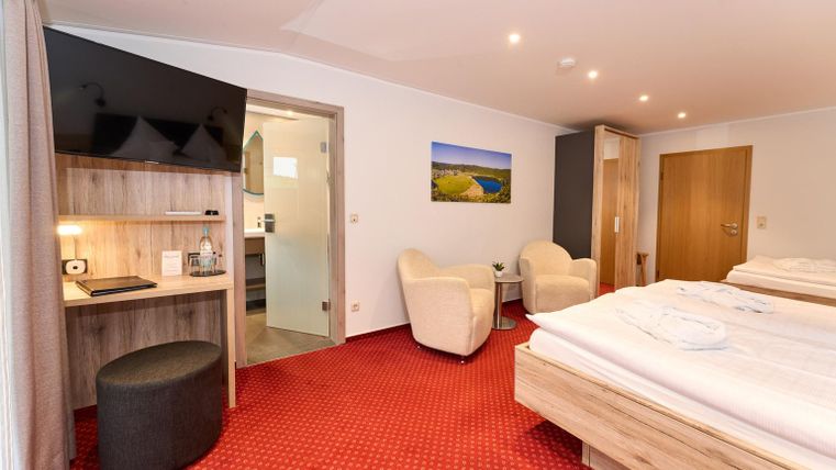 Een moderne hotelkamer met twee bedden, een televisie en een kleine bureau. De kleuren zijn warm en uitnodigend, met een comfortabele zithoek.