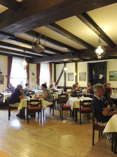 Ein gemütliches Restaurant mit Holzbalkendecke. Die Tische sind sauber gedeckt und Gäste genießen ihre Mahlzeiten.